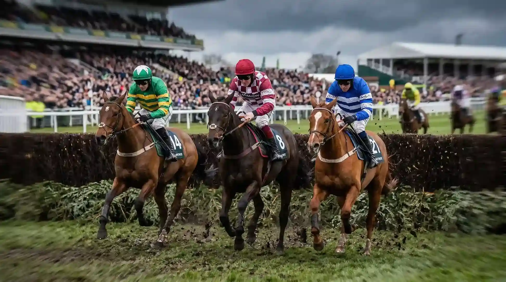 Three Grand National horses racing side by side over an Aintree fence